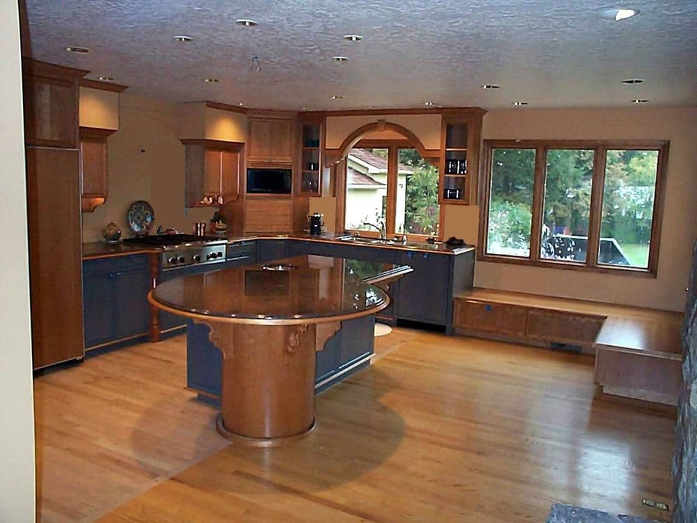 Modern kitchen with wooden cabinetry, large island, and bright windows overlooking greenery.