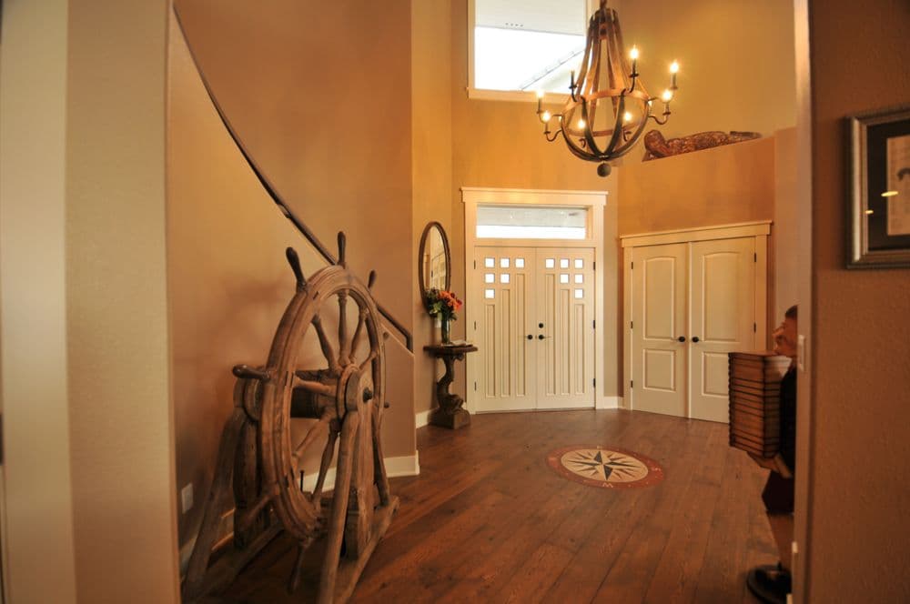 Welcoming foyer with wooden ship's wheel, chandelier, and decorative compass on the floor.
