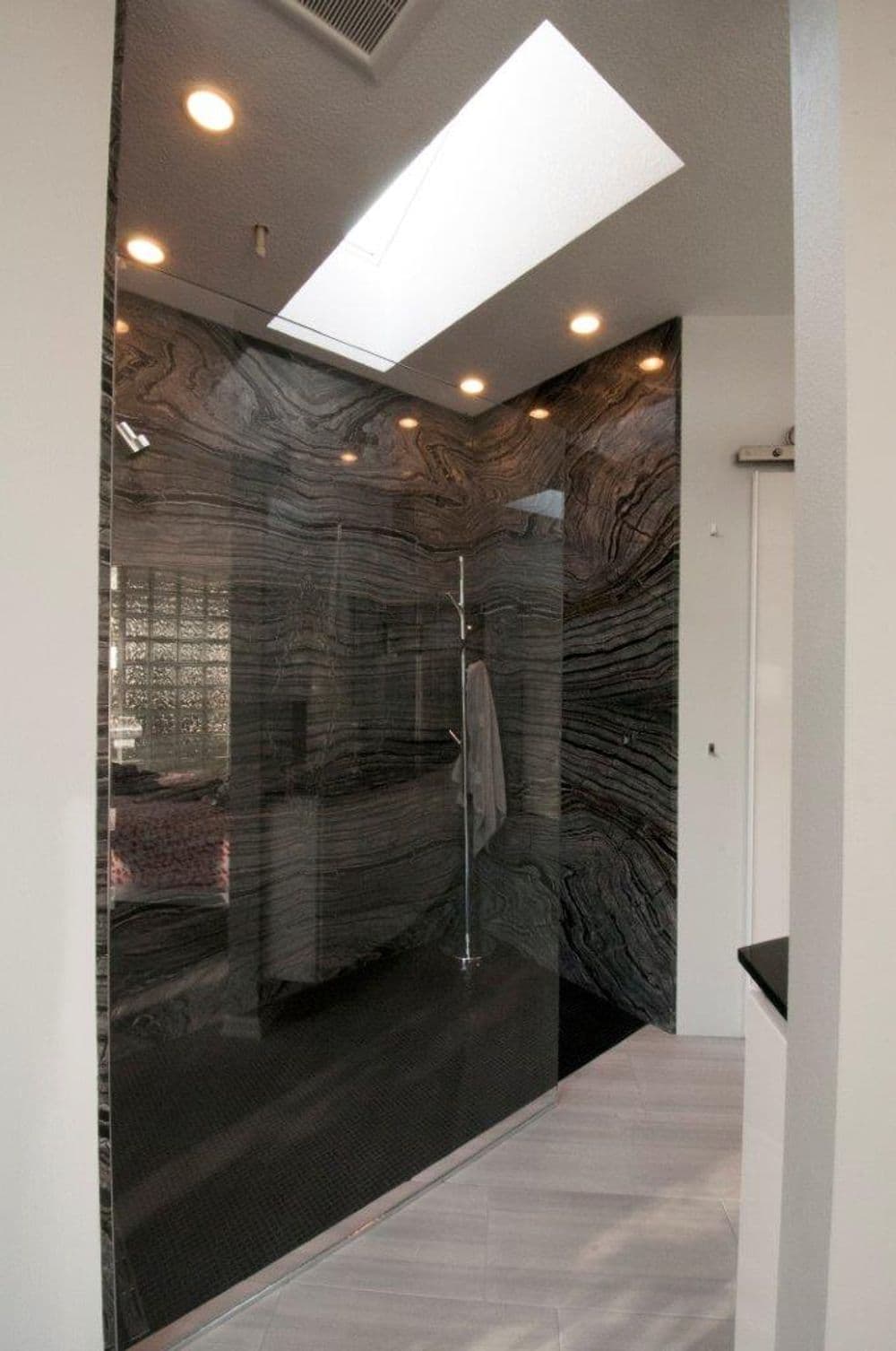 Modern walk-in shower with black marble walls, skylight, and sleek lighting.