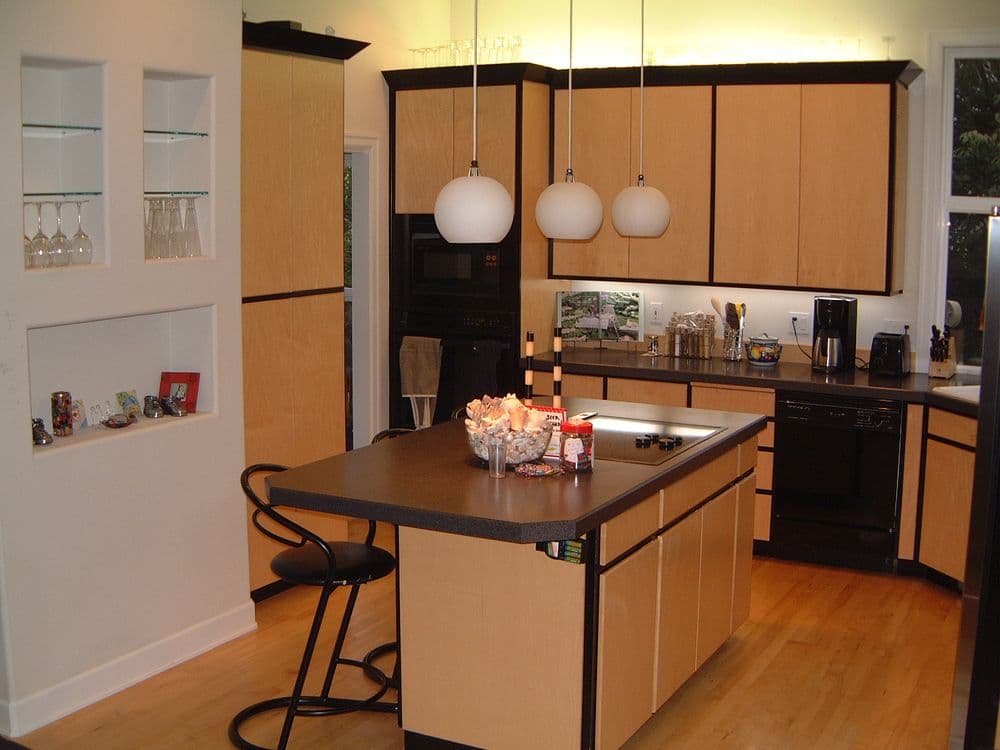 Modern kitchen with light wood cabinetry, black countertops, and an island with seating.