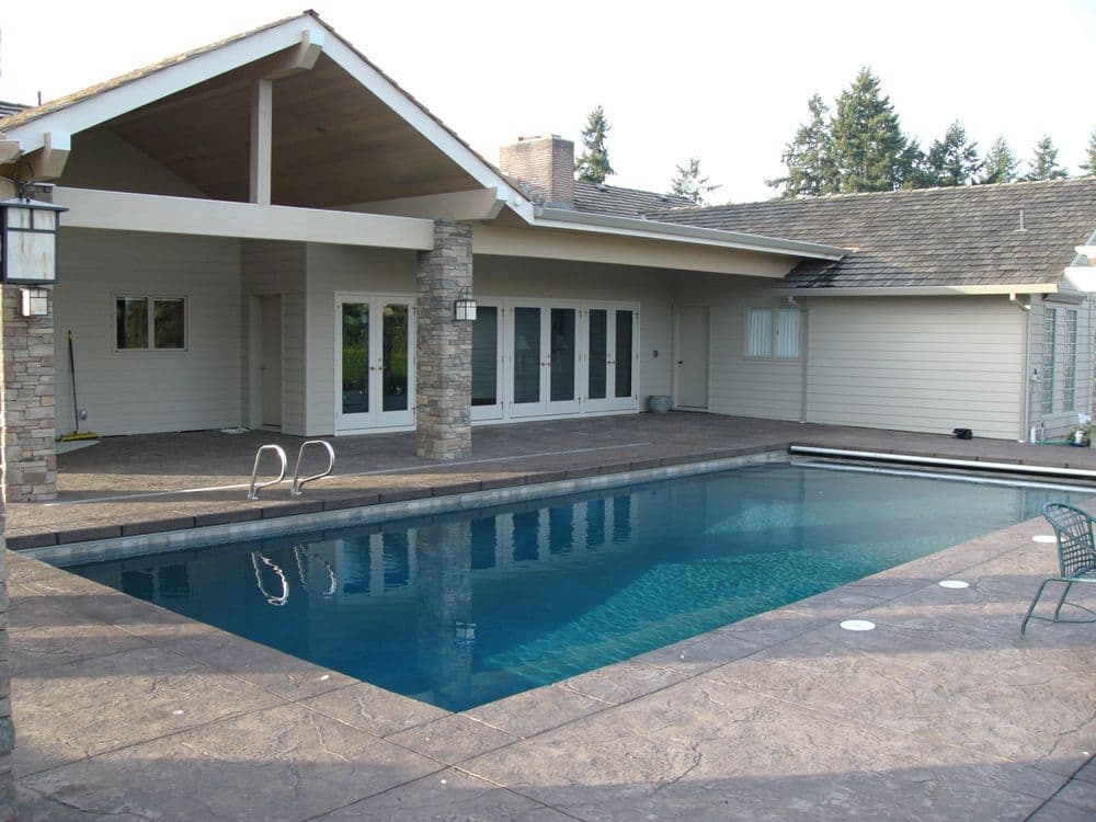 Modern home exterior featuring a swimming pool, patio area, and lush green surroundings.