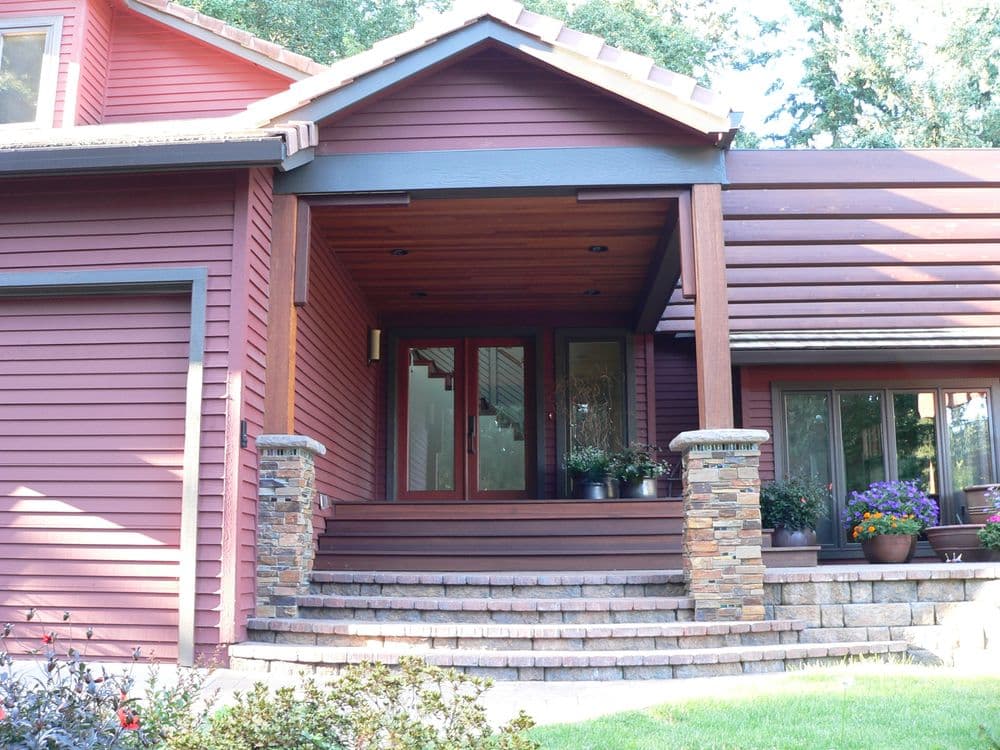 Modern red house entrance with stone pillars and landscaped steps. Bright, inviting design.