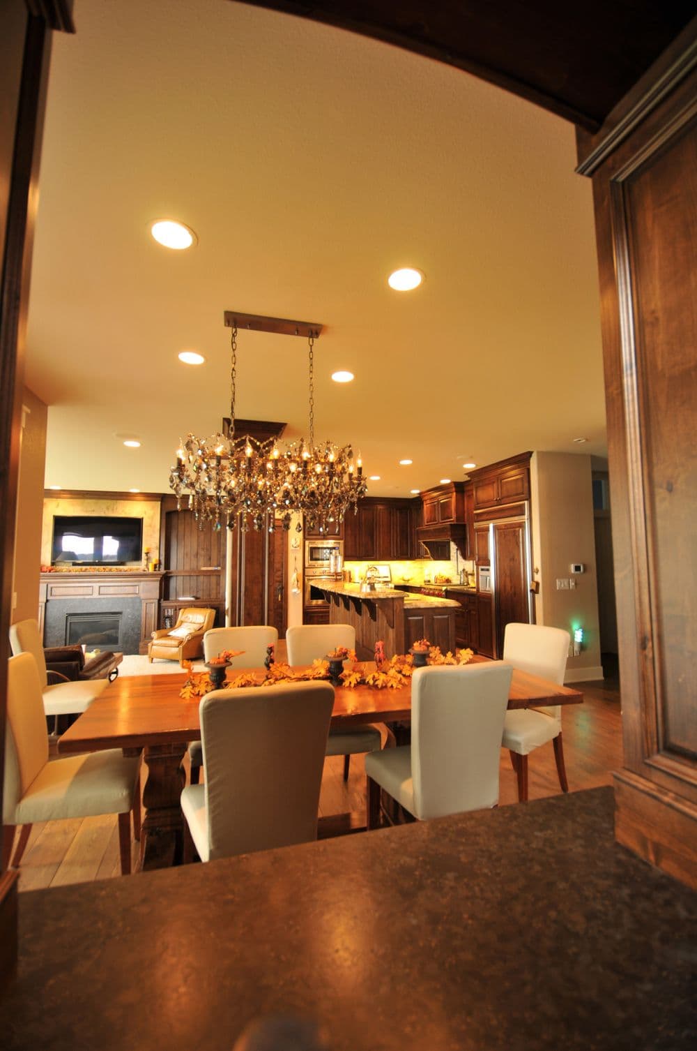 Elegant dining area with chandelier, wooden table, and autumn decor in a modern kitchen setting.
