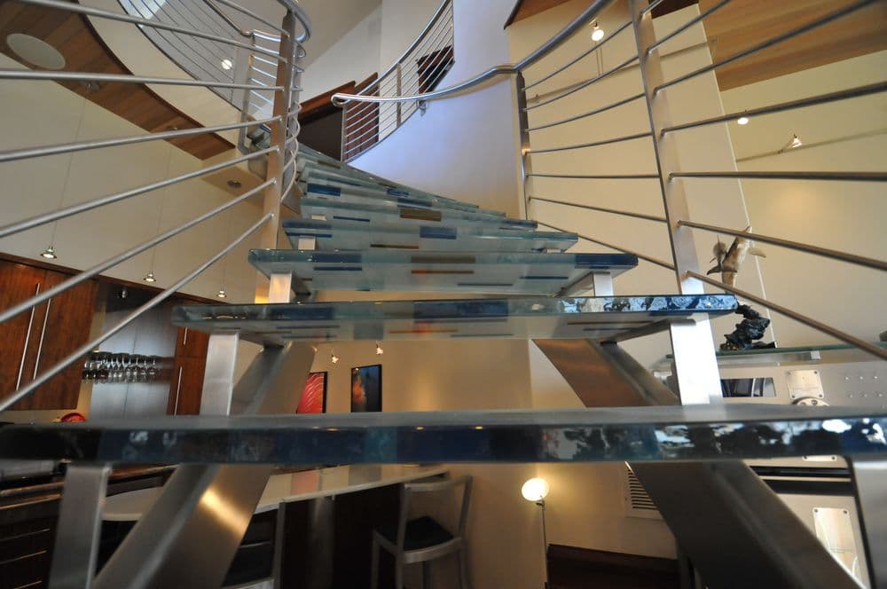 Modern spiral staircase with glass steps and sleek metal railing in contemporary home interior.