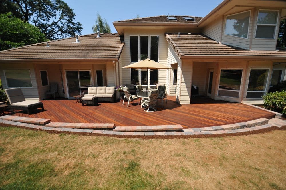 Spacious backyard deck with seating and a shade umbrella next to a modern home.