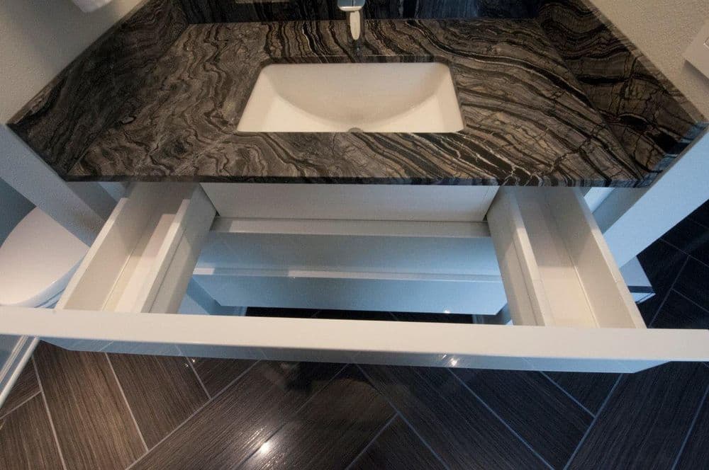 Modern bathroom vanity with a gray stone countertop and open drawer, showcasing storage space.