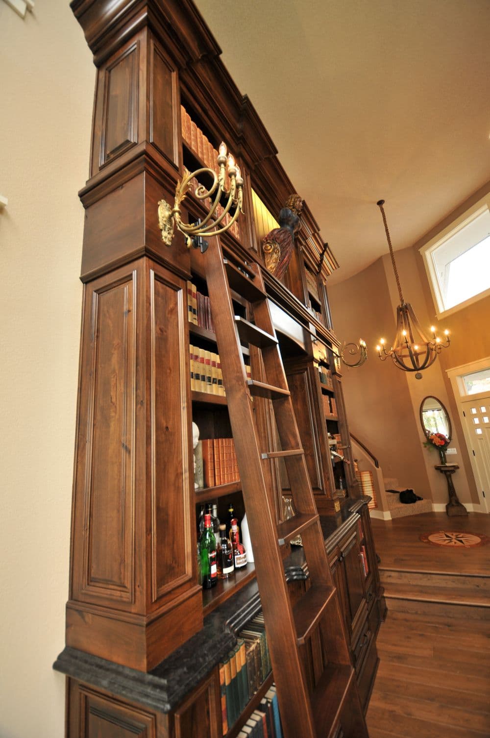 Elegant wooden bookshelf with a sliding ladder and decorative candelabra, in a spacious foyer.
