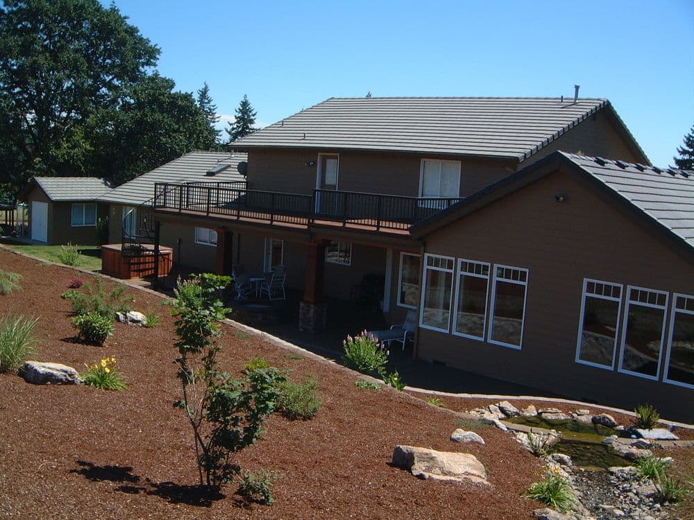 Modern two-story home with landscaped garden and patio, surrounded by trees and natural scenery.