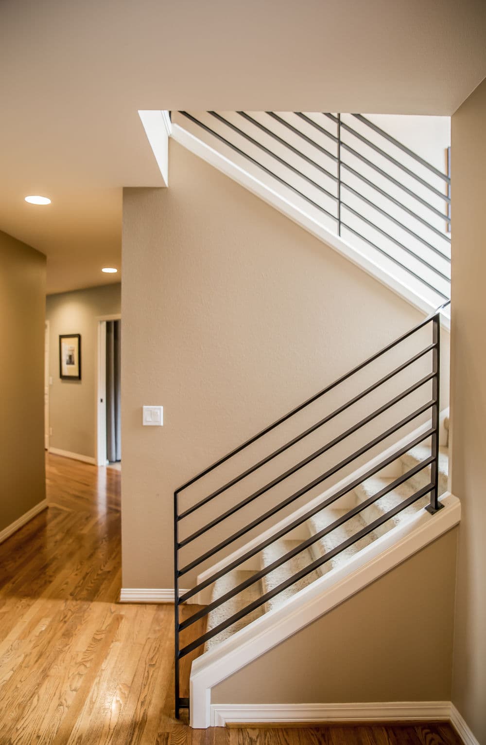 Modern staircase with black metal railing and warm wooden flooring in a bright interior.