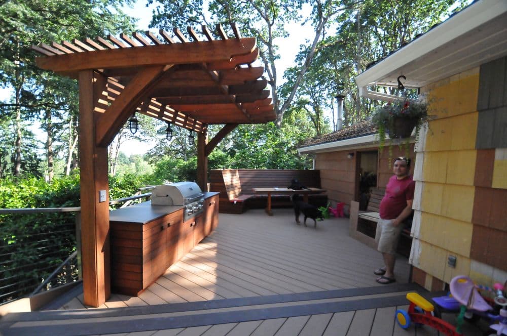 Outdoor patio with wooden pergola, grill area, seating, and a man standing beside a dog.