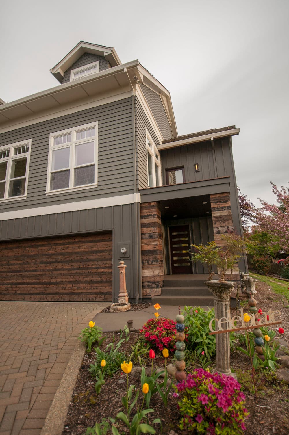 Modern home exterior with gray siding, landscaped garden, and colorful tulips in bloom.