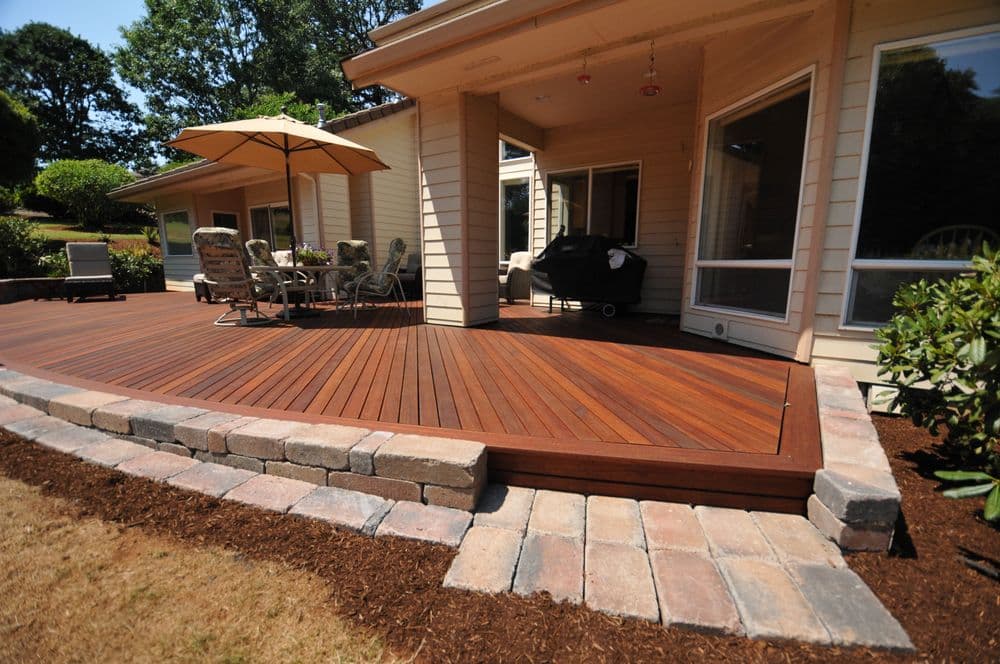 Stylish wooden deck with patio furniture and umbrella in a landscaped backyard setting.