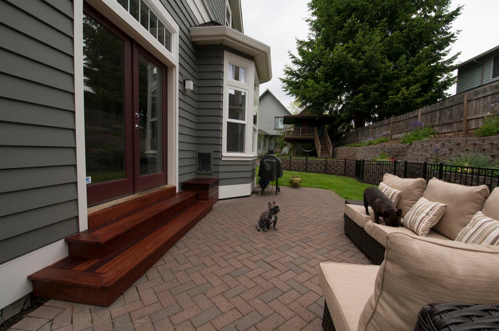 Cozy patio featuring a sectional sofa, dogs, and landscaped yard with steps and grill.