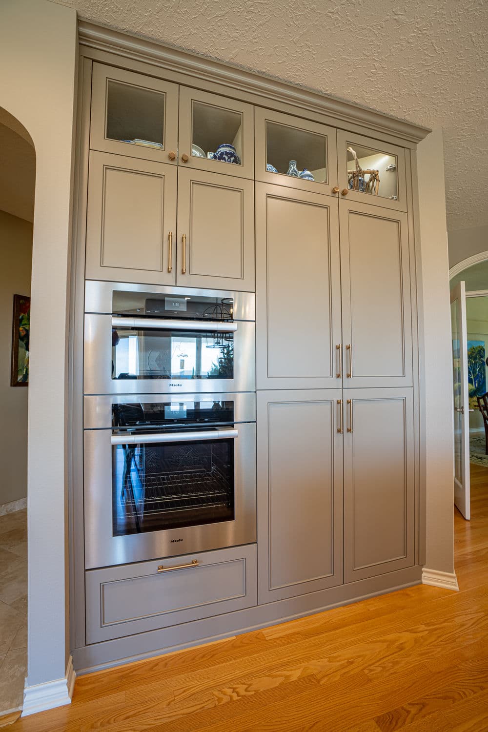 Modern kitchen cabinetry with built-in oven and glass-front storage. Elegant gray finish.