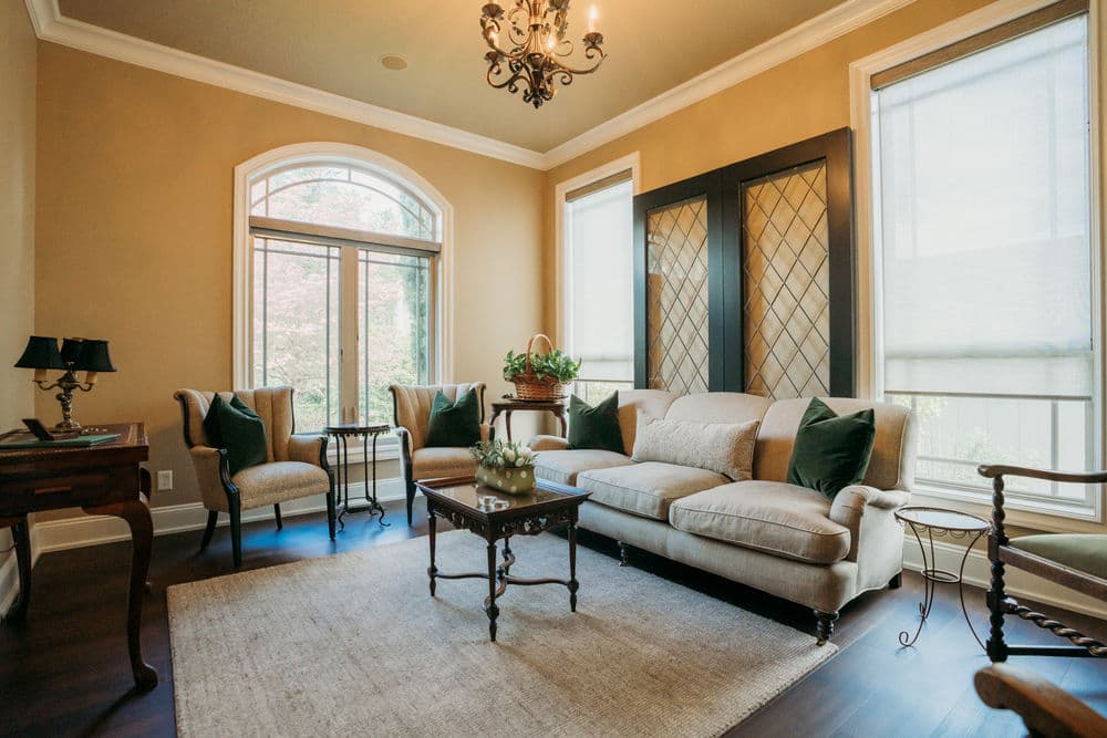 Cozy living room with beige walls, elegant furniture, and natural light through large windows.