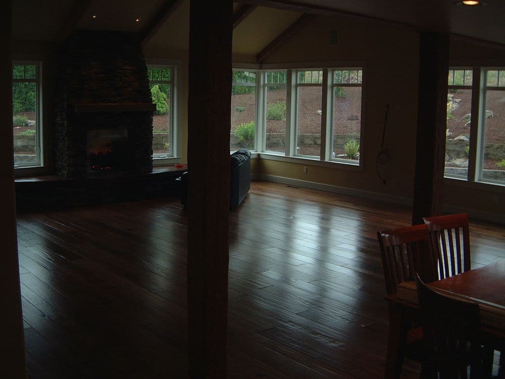 Cozy interior with wooden floors, stone fireplace, and large windows in a modern living room.