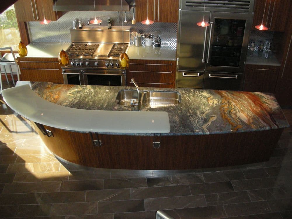 Modern kitchen featuring a curved granite countertop, stainless steel appliances, and pendant lighting.