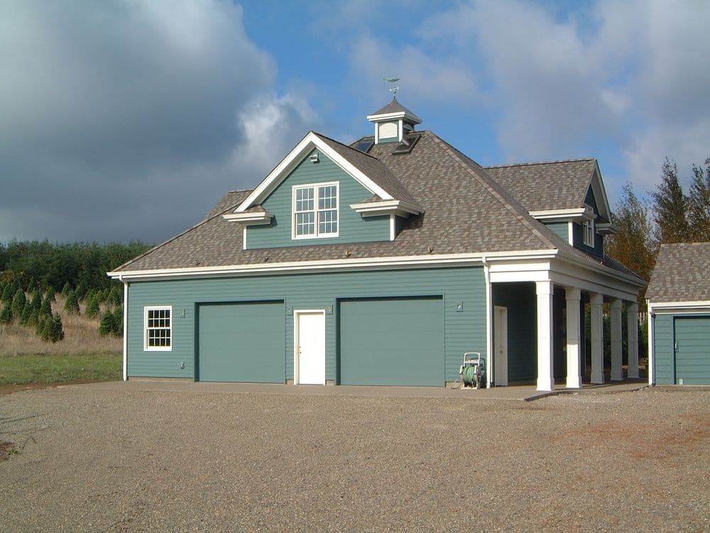 Modern blue garage with multiple doors, featuring a cupola and surrounded by gravel driveway.