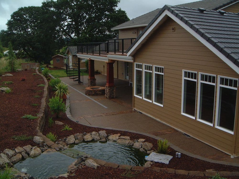 Modern house exterior with stone accents, lush landscaping, and a serene pond.