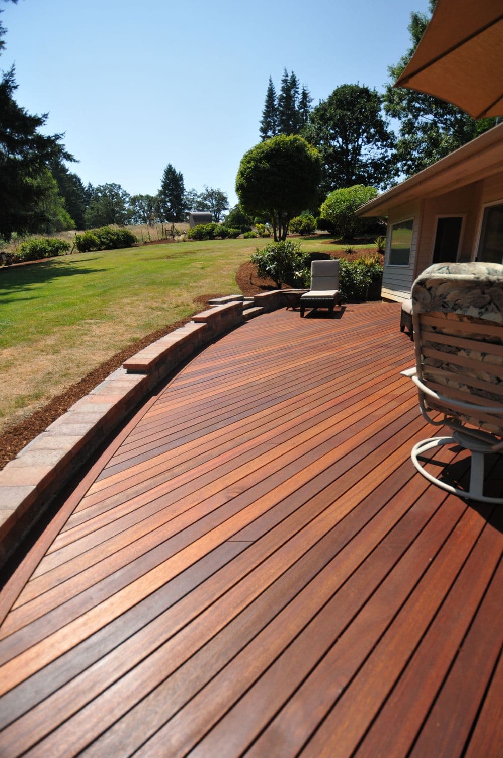 Beautiful wooden deck overlooking a green lawn and trees on a sunny day.
