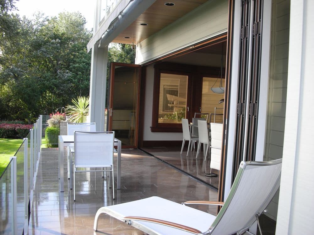 Modern outdoor patio with white furniture, overlooking a lush green garden.