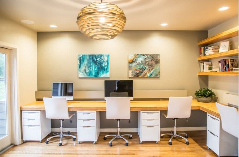 Modern home office with sleek design, two computers, and vibrant artwork on the wall.