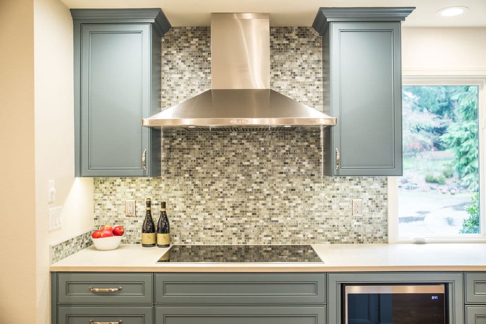 Modern kitchen with gray cabinets, stainless steel range hood, and mosaic tile backsplash.